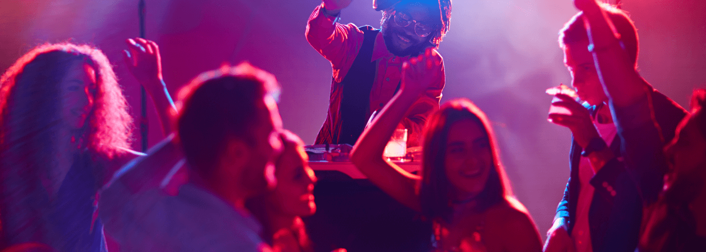 Live music performance with artist on stage and energized crowd with hands raised under vibrant purple and red stage lighting