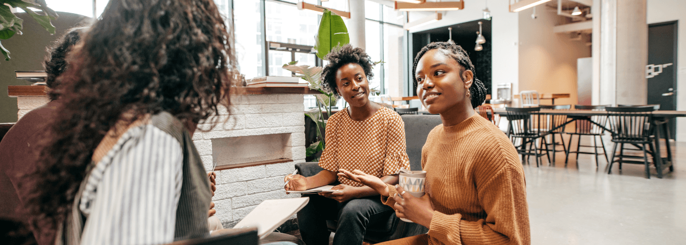 Three women engaged in collaborative learning discussion in modern bright study space with natural light